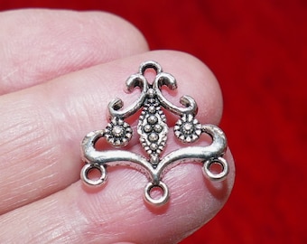 May include: A silver-colored metal jewelry finding with an ornate design. The piece features a central diamond shape with three small circles and two floral accents. It has three loops for attaching to other components.