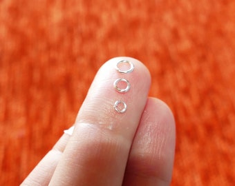 May include: Three silver jump rings of different sizes, lined up on a finger.