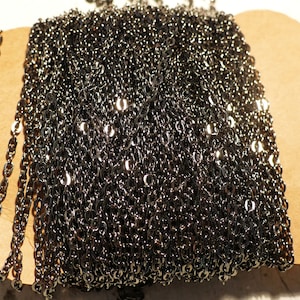 May include: A close-up of a black chain, likely made of metal. The chain is coiled and appears to be a bulk quantity.