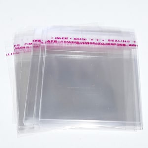 Puede incluir: Una pila de bolsas de pl&aacute;stico transparentes con una etiqueta rosa y blanca que dice "OKER BRAND *** SEALING TAPE ARE REMOVABLE INNER PROTECT EXPOSB ASH", la etiqueta est&aacute; en la parte superior de la pila de bolsas.