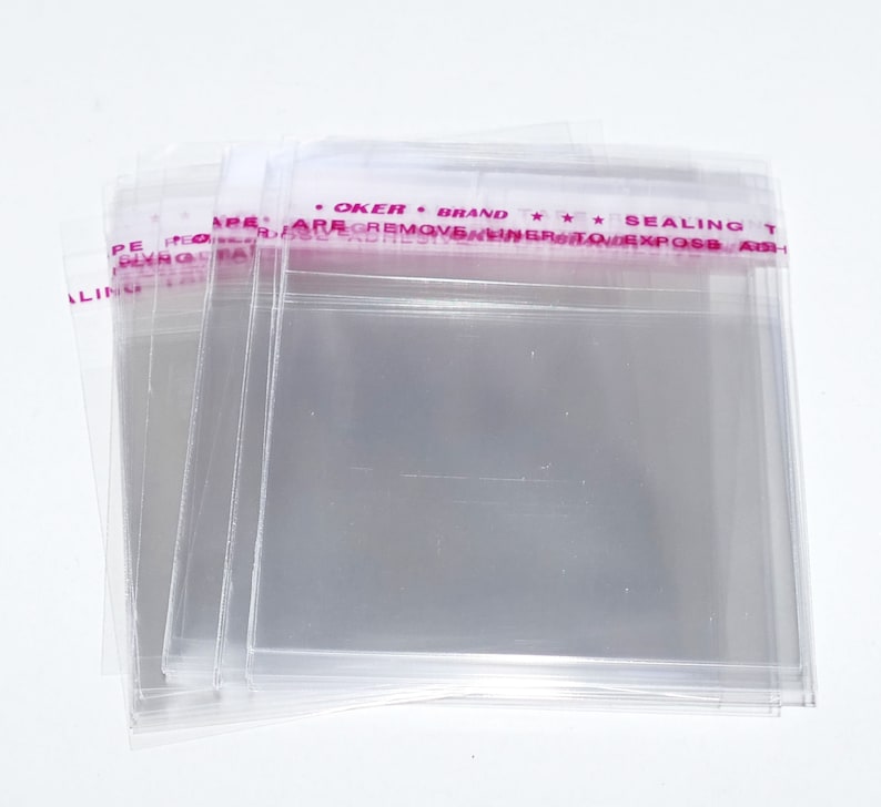 Puede incluir: Una pila de bolsas de pl&aacute;stico transparentes con una etiqueta rosa y blanca que dice "OKER BRAND *** SEALING TAPE ARE REMOVABLE INNER PROTECT EXPOSB ASH", la etiqueta est&aacute; en la parte superior de la pila de bolsas.
