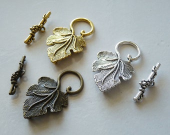 May include: Three sets of decorative metal leaf-shaped clasps with a vine design. Each clasp has a matching bar with a grape cluster design. The clasps are in gold, silver, and antique bronze.