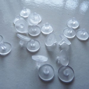 May include: A close-up of a pile of clear plastic furniture protectors. The protectors are round with a small raised center. They are designed to prevent scratches and damage to furniture.