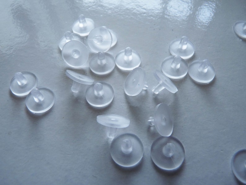 May include: A close-up of a pile of clear plastic furniture protectors. The protectors are round with a small raised center. They are designed to prevent scratches and damage to furniture.