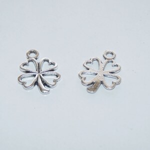 May include: Two silver four-leaf clover charms with a loop at the top for attaching to jewelry or other crafts.