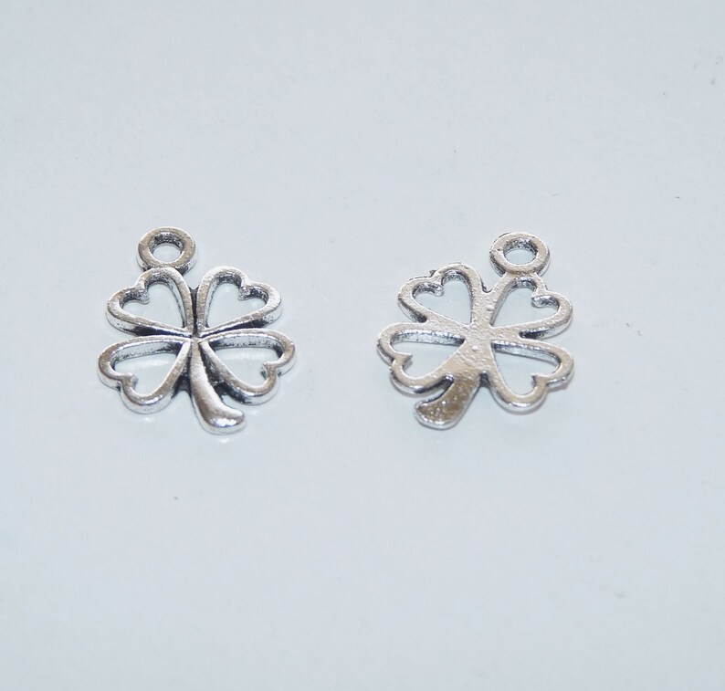 May include: Two silver four-leaf clover charms with a loop at the top for attaching to jewelry or other crafts.