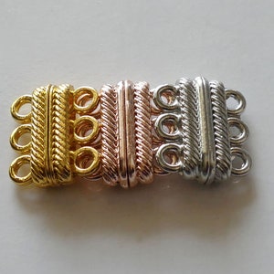 Könnte beinhalten: Drei Metallverschlüsse für Halsketten oder Armbänder. Die Verschlüsse sind in Gold-, Roségold- und Silbertönen gehalten. Jeder Verschluss hat drei Schlaufen zum Anbringen von Schmuck.