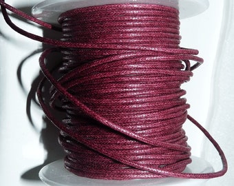 May include: A spool of burgundy waxed cotton cord. The cord is wound tightly around the spool, creating a thick, textured look.
