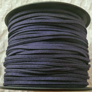 May include: A spool of dark purple suede cord. The cord is wound tightly around a black plastic spool.