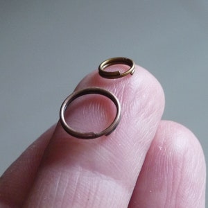 Puede incluir: Dos pequeños anillos de salto redondos de metal. Los anillos son de diferentes tamaños y se muestran en un dedo.