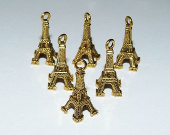 Puede incluir: Seis abalorios de color dorado en forma de Torre Eiffel con un bucle en la parte superior para sujetarlos a joyas u otras manualidades.