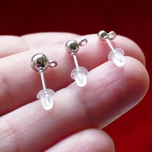 May include: Three silver earring posts with clear plastic stoppers. The posts are round and have a small loop at the top.