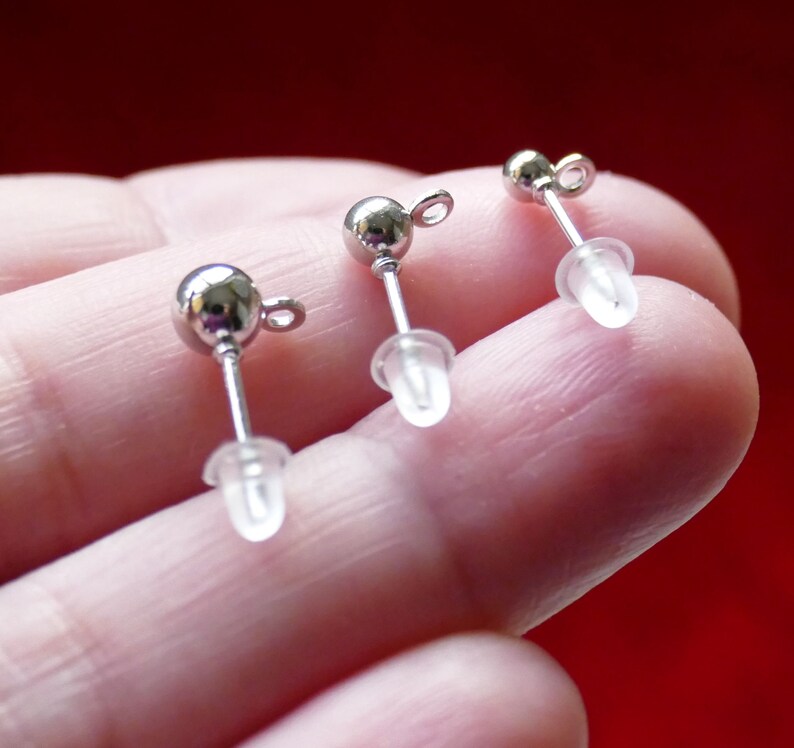 May include: Three silver earring posts with clear plastic stoppers. The posts are round and have a small loop at the top.