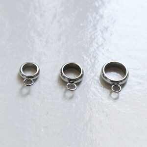 Peut inclure: Trois anneaux de saut en argent avec une petite boucle en bas. Les anneaux sont de tailles diff&eacute;rentes.