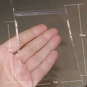 Może przedstawiać: Przezroczysta plastikowa torebka z taśmą uszczelniającą z napisem "CHENG JIA * SEALING TAPE REMOVE LINER". Torebka ma wymiary 9 cm x 7 cm x 12 cm.