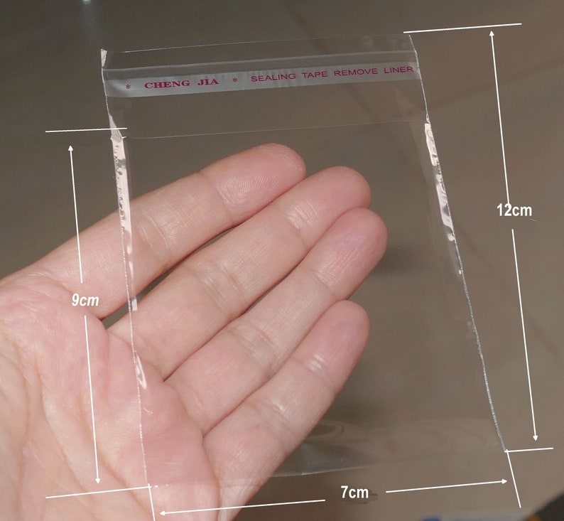 Może przedstawiać: Przezroczysta plastikowa torebka z taśmą uszczelniającą z napisem "CHENG JIA * SEALING TAPE REMOVE LINER". Torebka ma wymiary 9 cm x 7 cm x 12 cm.