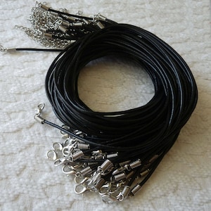 May include: A bulk pack of black leather cord necklaces with silver lobster clasps. The cords are coiled together and the clasps are scattered around the cords.