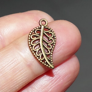May include: A bronze leaf charm with detailed openwork and a small loop. The leaf design has a central vein and decorative patterns, ideal for jewellery making or craft projects.