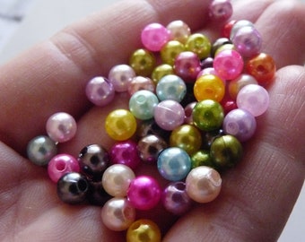 May include: A collection of colorful pearl beads in various shades of pink, purple, green, yellow, and brown. The beads are arranged in a hand, showcasing their iridescent sheen.