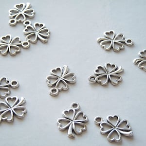 May include: A collection of silver-toned metal charms shaped like four-leaf clovers. Each charm has a loop at the top for attaching to jewelry or other crafts.