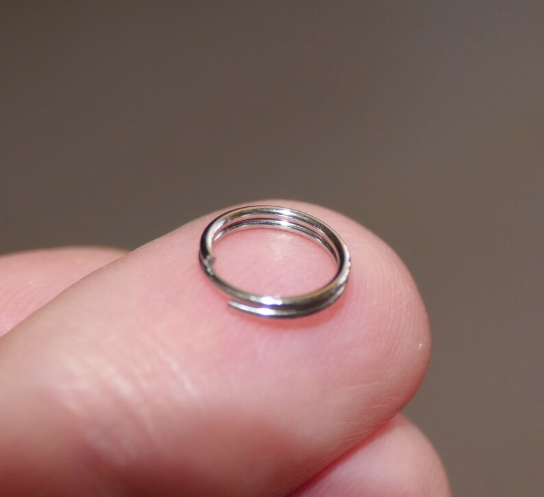Puede incluir: Un anillo de salto plateado, un peque&ntilde;o anillo de metal utilizado para conectar componentes de joyer&iacute;a.
