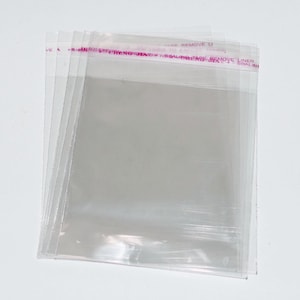 Może przedstawiać: Stos przezroczystych plastikowych torebek z r&oacute;żową taśmą klejącą, na kt&oacute;rej widnieje napis "CARE REMOVE LINER BEFORE SEALING TAPE REMOVE LINER SEALING TAPE".