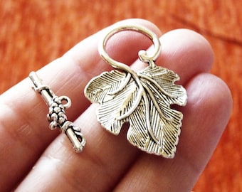 May include: Silver tone leaf-shaped toggle clasp with a grapevine design. The clasp is made of metal and has a shiny finish.