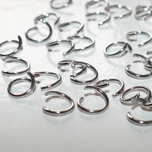 May include: A close-up of a group of silver hoop earrings. The earrings are all the same size and shape, and they are arranged in a random pattern on a white surface.