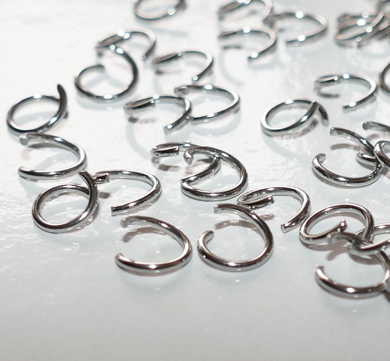 May include: A close-up of a group of silver hoop earrings. The earrings are all the same size and shape, and they are arranged in a random pattern on a white surface.