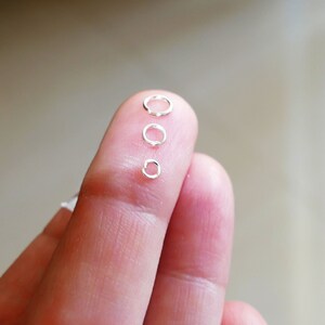 May include: Four silver jump rings of different sizes, arranged in order from largest to smallest, on a finger.