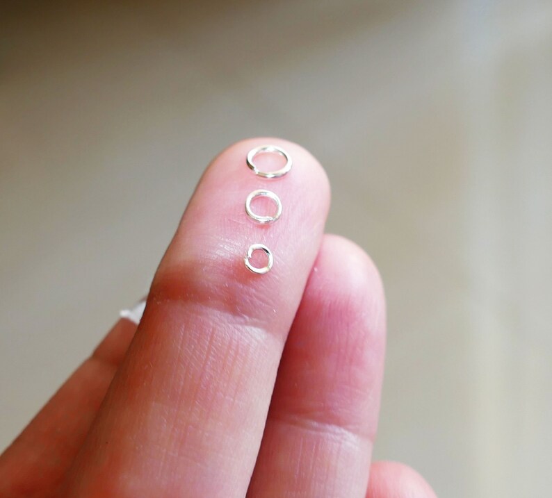 May include: Four silver jump rings of different sizes, arranged in order from largest to smallest, on a finger.