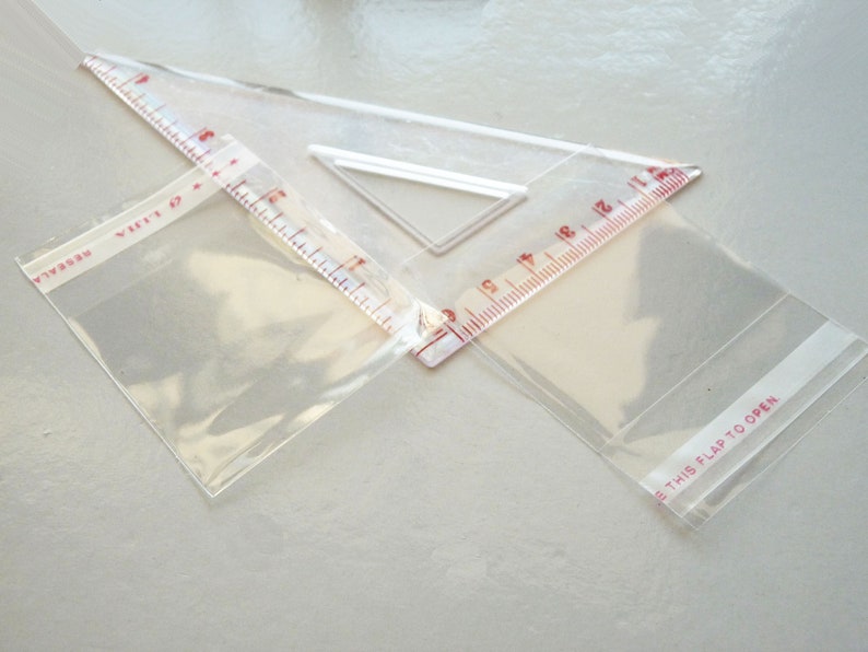 May include: Two clear plastic bags with red printed text. One bag has the text "Resealable" and the other has the text "This flap to open". A clear plastic ruler with red markings is on top of the bags.