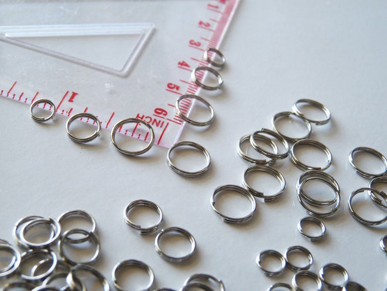 May include: A large quantity of silver jump rings of various sizes. The rings are scattered on a white surface.