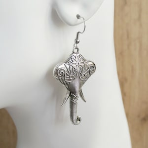 Puede incluir: Pendientes de plata con forma de elefante con detalles intrincados. Los pendientes son colgantes y tienen un diseño floral en la cabeza del elefante.
