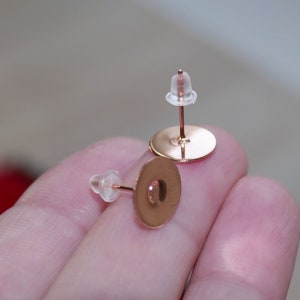 Könnte beinhalten: Zwei goldfarbene Ohrring-Stifte mit durchsichtigen Kunststoff-Rücken.
