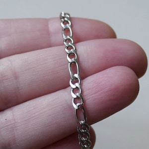 Può includere: Una collana a catena d'argento con un motivo a maglia figaro.