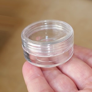 Può includere: Un contenitore di plastica trasparente con un coperchio a vite. Il contenitore è vuoto e sembra essere fatto di plastica resistente.