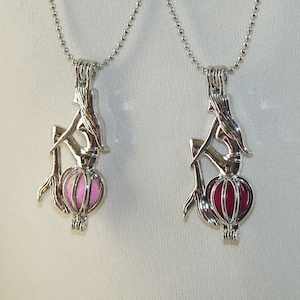 Peut inclure: Deux colliers en argent avec un pendentif en forme de sirène et une boule de verre. Un pendentif est rempli de paillettes roses et l'autre de paillettes rouges.