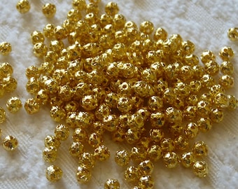 May include: A large pile of gold-colored metal beads with a textured surface. The beads are round and have a small hole in the center.