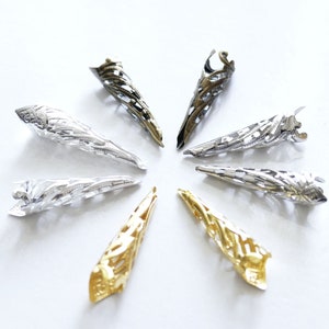 Könnte beinhalten: Sieben verzierte Metallspitzen in Gold, Silber und antikem Silber. Die Spitzen sind kegelförmig mit einem dekorativen, filigranen Design.