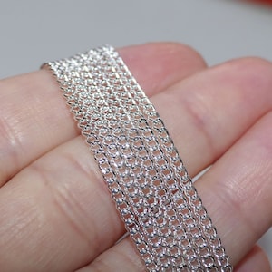 Può includere: Un ciondolo a catena d'argento. La catena è composta da piccoli anelli intrecciati. La catena è mostrata in più strati, evidenziando il suo design delicato.