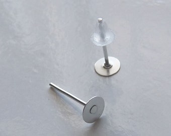 May include: Two silver earring posts with clear plastic stoppers. The posts have a flat round base.