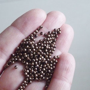 May include: A pile of small, round, bronze-coloured beads in a hand. The beads have a hole in the centre.