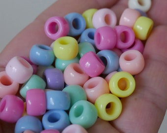 Puede incluir: Una colección de cuentas de plástico de colores pastel en varios tonos de rosa, azul, amarillo y verde. Las cuentas son redondas y tienen un agujero en el centro para enhebrar.