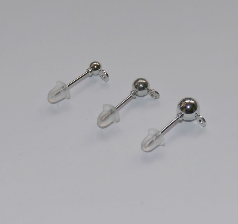 May include: Three silver earring posts with clear rubber backs. The posts are different lengths.