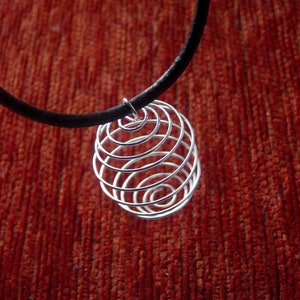 Può includere: Una collana in metallo argentato con un ciondolo a spirale. La collana è su una superficie rossa testurizzata.