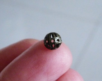 May include: A small, round, metal bead with a decorative, openwork design. The bead is silver in color and has a slightly textured surface.