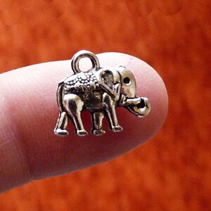 K&ouml;nnte beinhalten: Ein silberner Anh&auml;nger in Form eines Elefanten. Der Elefant hat eine strukturierte Oberfl&auml;che und eine Schlaufe oben zum Anbringen an einer Kette oder einem Armband.