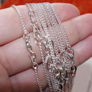 Può includere: Primo piano di un set di catene d'argento con chiusure a moschettone. Le catene sono disposte a ventaglio e sono tenute in una mano.