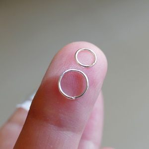 May include: Two silver jump rings, one larger than the other, are held on a finger.